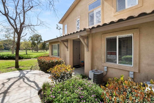 view of exterior entry featuring a yard, cooling unit, and a patio area