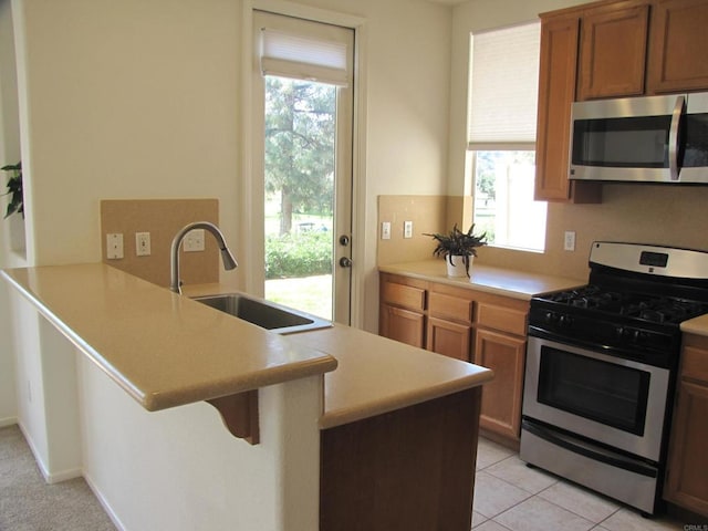 kitchen with sink, a kitchen bar, kitchen peninsula, stainless steel appliances, and light tile patterned floors