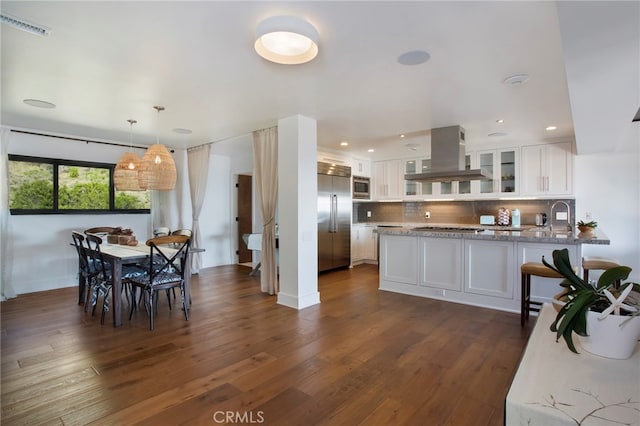 kitchen featuring white cabinets, backsplash, built in appliances, dark hardwood / wood-style flooring, and island exhaust hood