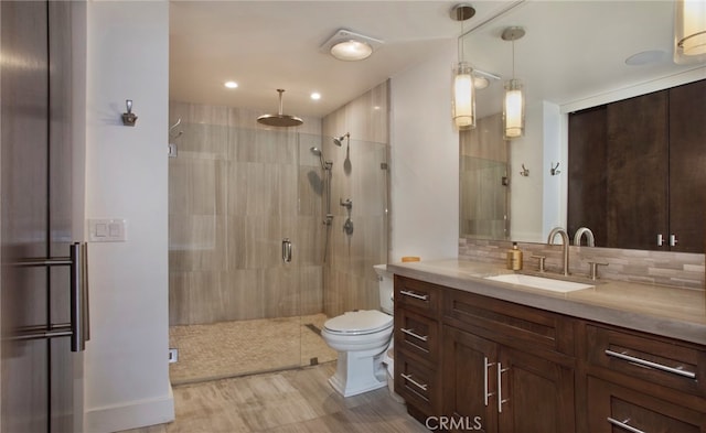 bathroom with a shower with shower door, vanity, toilet, and tasteful backsplash