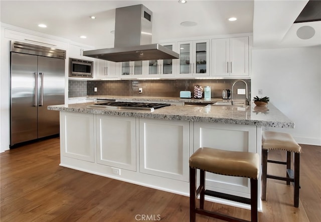 kitchen with dark hardwood / wood-style floors, built in appliances, white cabinets, island range hood, and decorative backsplash