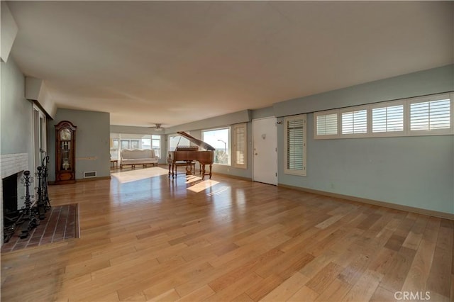 unfurnished living room with light wood-style floors, a brick fireplace, visible vents, and baseboards