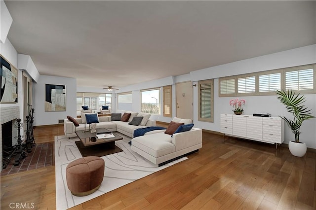 living room featuring a brick fireplace, ceiling fan, baseboards, and wood finished floors