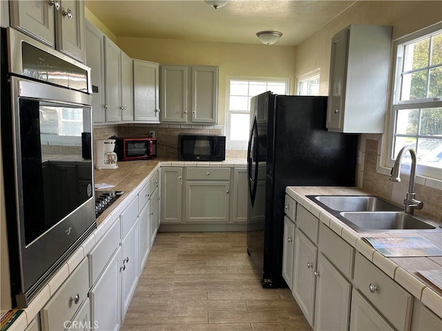 kitchen featuring black appliances, a wealth of natural light, light wood-type flooring, and tile counters