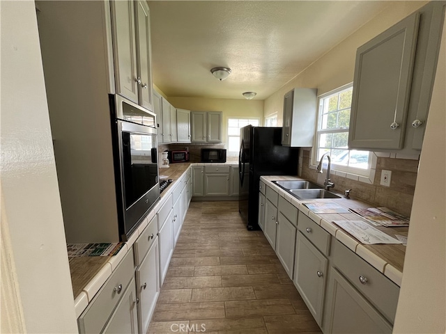 kitchen with tasteful backsplash, black appliances, sink, light wood-type flooring, and tile counters