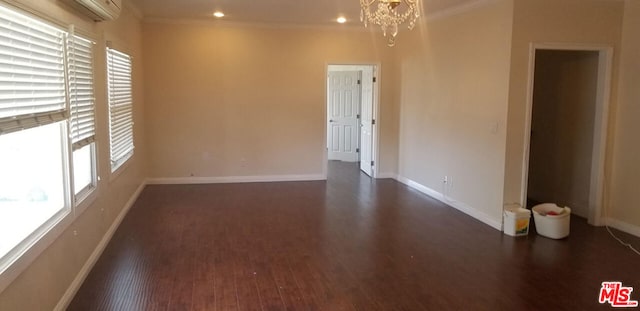 empty room featuring an inviting chandelier, ornamental molding, a wall mounted AC, and dark hardwood / wood-style flooring