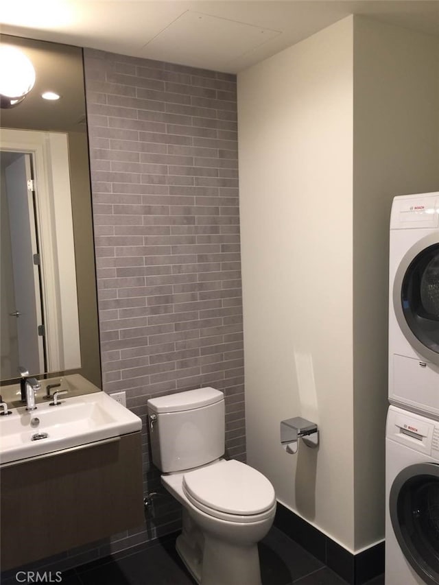 bathroom featuring tile walls, toilet, sink, tile floors, and stacked washer and clothes dryer