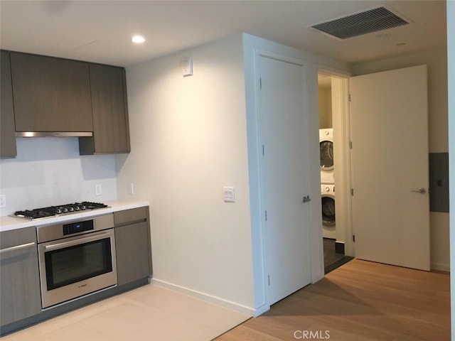 kitchen featuring appliances with stainless steel finishes, gray cabinets, stacked washer / drying machine, and light hardwood / wood-style flooring