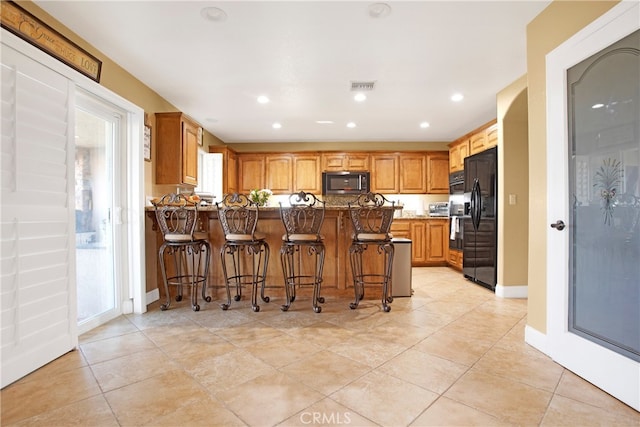 kitchen with light tile patterned flooring, black fridge with ice dispenser, a kitchen bar, and kitchen peninsula