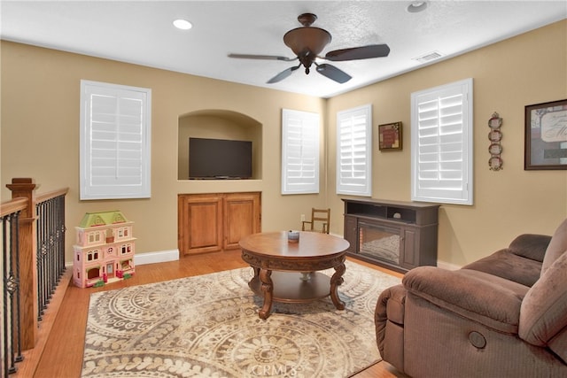 living room featuring ceiling fan, light wood-type flooring, and a fireplace