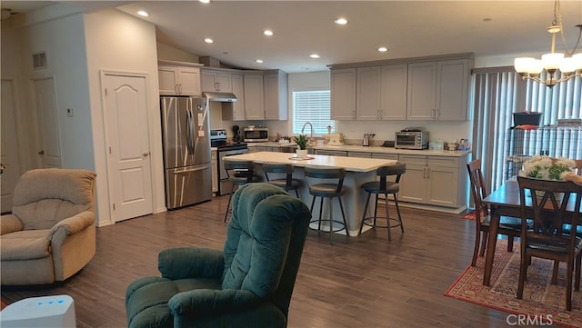 kitchen featuring a breakfast bar area, appliances with stainless steel finishes, vaulted ceiling, dark hardwood / wood-style floors, and pendant lighting