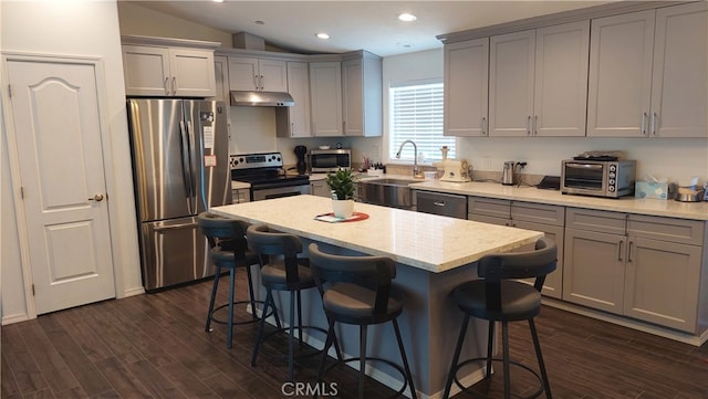 kitchen featuring dark wood-type flooring, gray cabinetry, a center island, vaulted ceiling, and appliances with stainless steel finishes