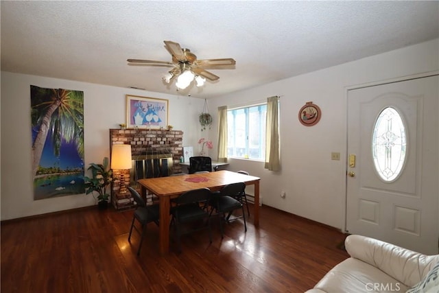 dining area with a textured ceiling, ceiling fan, dark wood-type flooring, and a brick fireplace