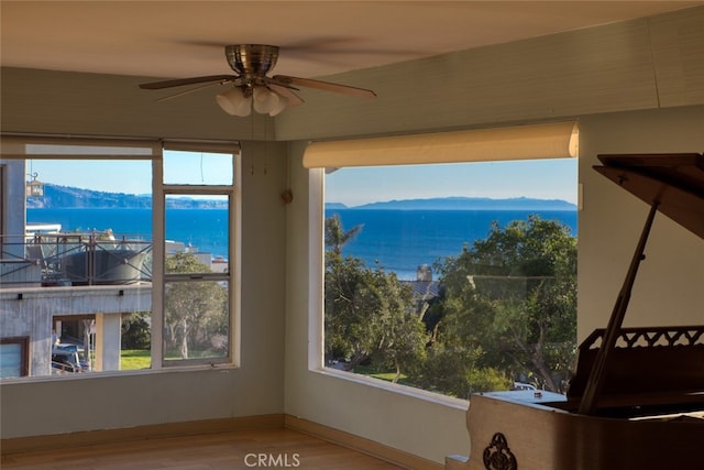 interior space with a water and mountain view, ceiling fan, and hardwood / wood-style flooring