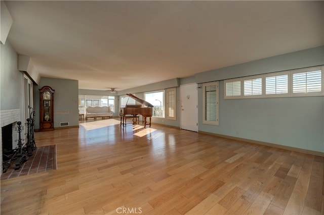 unfurnished living room featuring a brick fireplace, ceiling fan, and light wood-type flooring