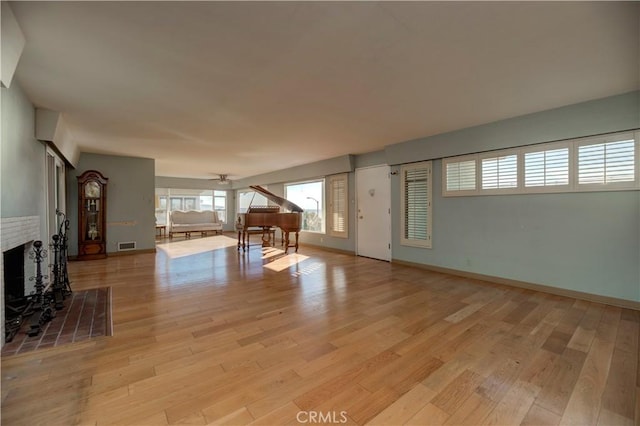 unfurnished living room with light wood-type flooring, a fireplace, visible vents, and baseboards