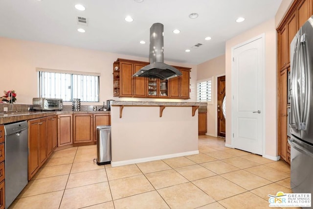 kitchen with island range hood, light tile patterned flooring, a breakfast bar area, and appliances with stainless steel finishes