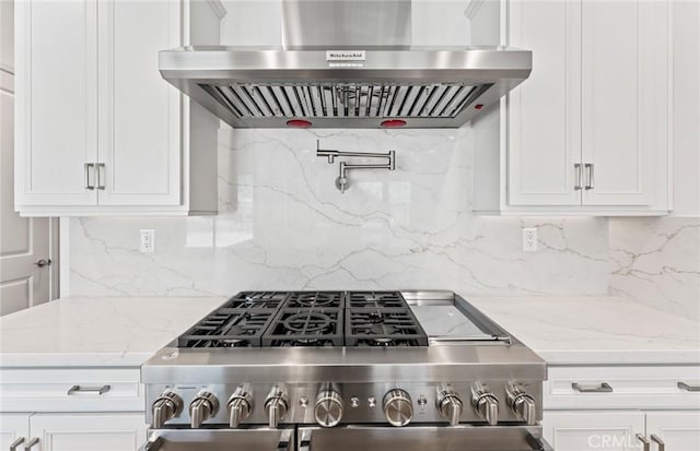 kitchen featuring light stone countertops, stainless steel range, wall chimney range hood, tasteful backsplash, and white cabinets