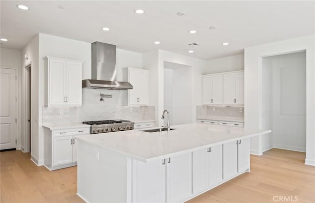 kitchen with a center island with sink, sink, light hardwood / wood-style flooring, wall chimney exhaust hood, and white cabinetry