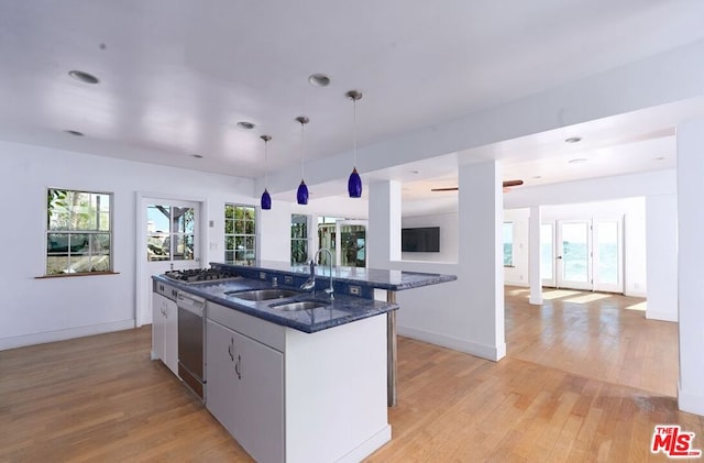 kitchen with pendant lighting, light hardwood / wood-style floors, a kitchen island with sink, sink, and appliances with stainless steel finishes