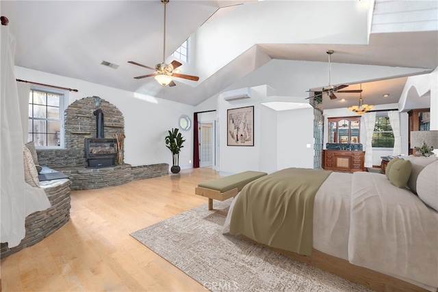 bedroom with hardwood / wood-style floors, a wood stove, a chandelier, high vaulted ceiling, and a wall mounted air conditioner