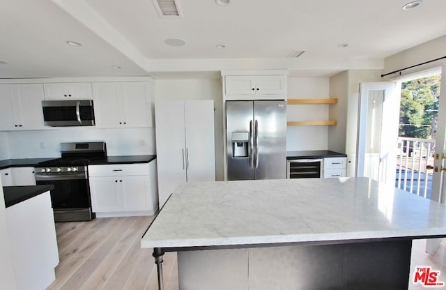 kitchen with a kitchen island, stainless steel appliances, beverage cooler, white cabinets, and light hardwood / wood-style floors