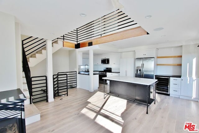 kitchen with stainless steel appliances, wine cooler, a center island, white cabinetry, and light hardwood / wood-style floors