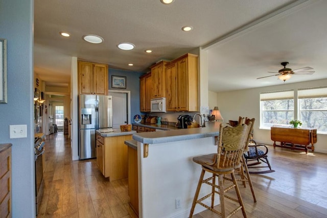 kitchen with a kitchen bar, kitchen peninsula, stainless steel appliances, a healthy amount of sunlight, and light wood-type flooring