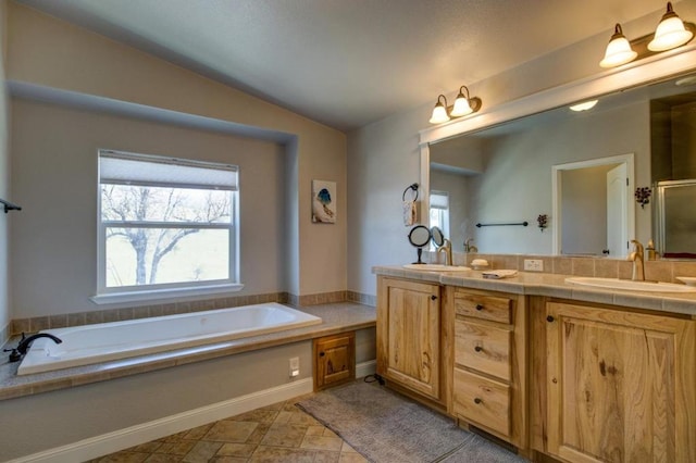 bathroom with vanity, a wealth of natural light, vaulted ceiling, and a tub