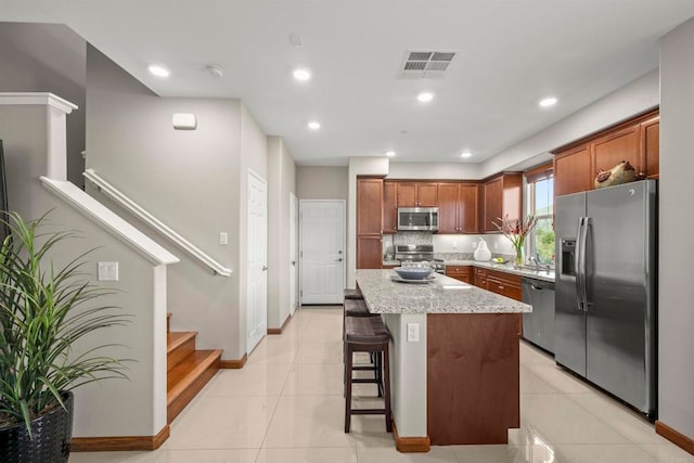 kitchen featuring a center island, appliances with stainless steel finishes, tasteful backsplash, light tile patterned flooring, and a kitchen bar