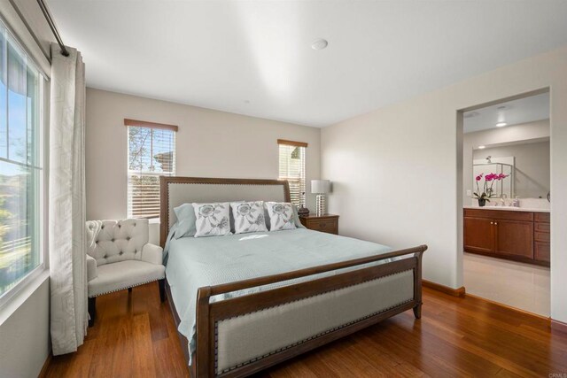 bedroom with multiple windows, ensuite bathroom, sink, and wood-type flooring