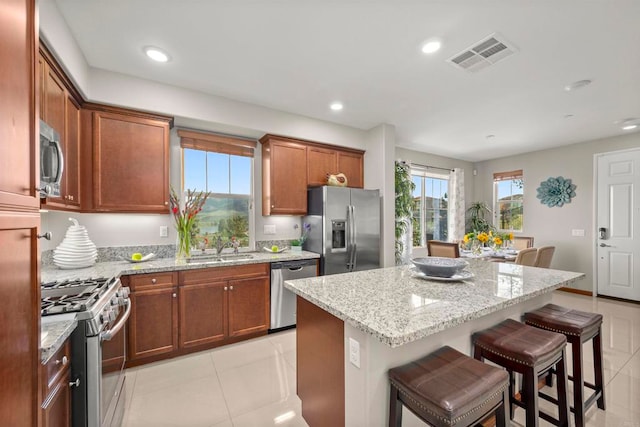 kitchen with light stone countertops, a center island, sink, a kitchen bar, and appliances with stainless steel finishes