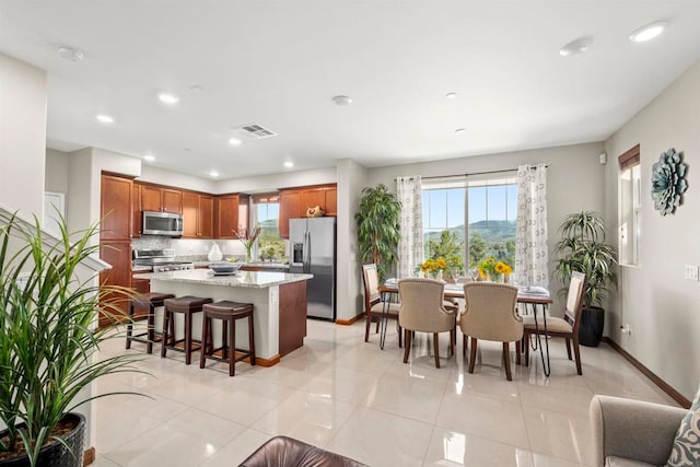 kitchen featuring light tile patterned floors, light stone counters, appliances with stainless steel finishes, a kitchen island, and a kitchen bar