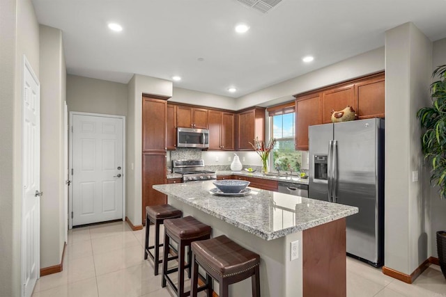 kitchen with light stone countertops, a center island, tasteful backsplash, a kitchen bar, and appliances with stainless steel finishes