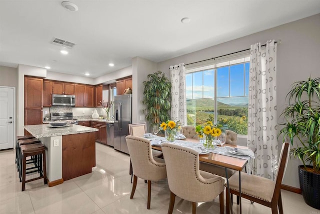 kitchen featuring a center island, stainless steel appliances, light stone counters, decorative backsplash, and light tile patterned floors