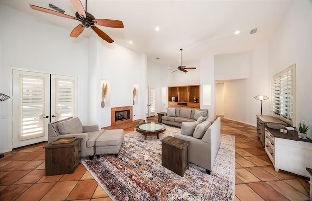 tiled living room featuring a tile fireplace, ceiling fan, french doors, and high vaulted ceiling