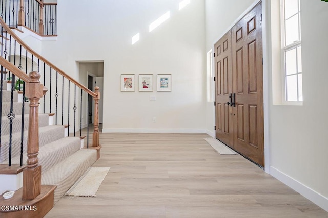 foyer with light wood-type flooring and a towering ceiling