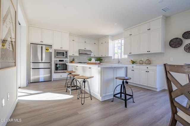 kitchen with decorative backsplash, white cabinetry, built in appliances, a kitchen bar, and light hardwood / wood-style flooring