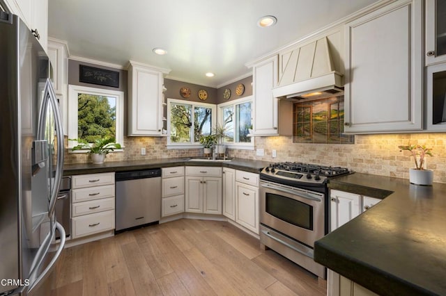 kitchen with stainless steel appliances, dark countertops, premium range hood, tasteful backsplash, and light wood-style floors