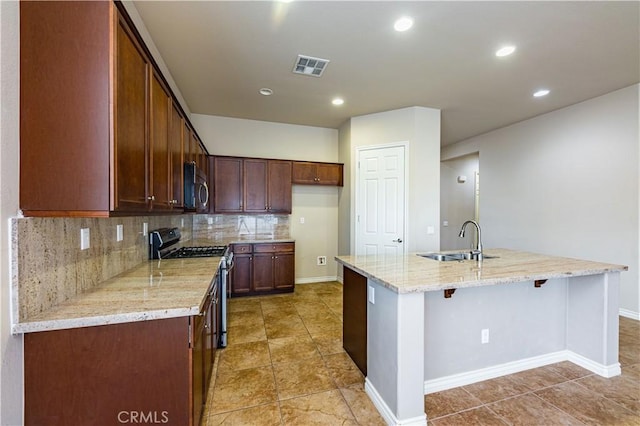 kitchen with sink, a center island with sink, stainless steel appliances, light stone countertops, and backsplash