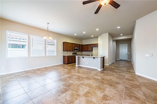 kitchen with pendant lighting, ceiling fan with notable chandelier, a breakfast bar, a center island with sink, and decorative backsplash