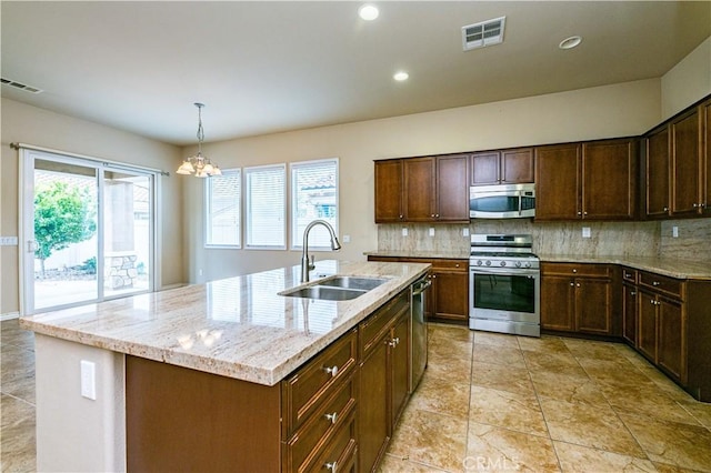 kitchen featuring appliances with stainless steel finishes, sink, decorative backsplash, a kitchen island with sink, and light stone counters