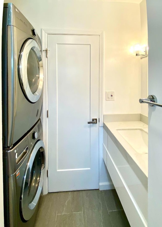 washroom featuring stacked washer and dryer and dark tile patterned floors