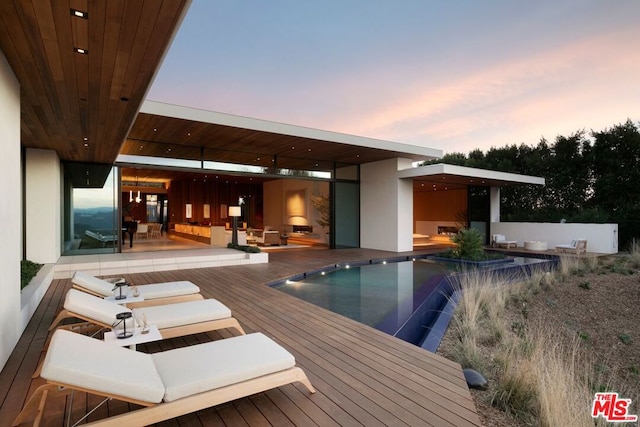 back house at dusk featuring a pool side deck and pool water feature