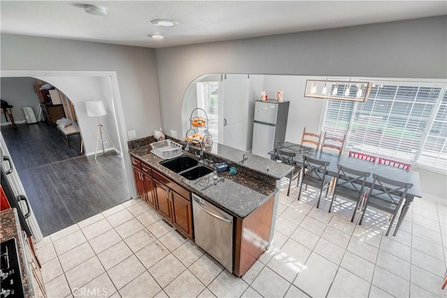 kitchen featuring dark stone countertops, sink, light tile patterned floors, and stainless steel appliances