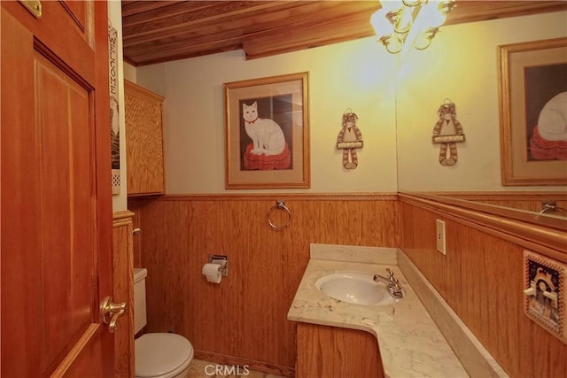 bathroom with toilet, wooden walls, wooden ceiling, and vanity