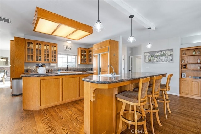 kitchen with sink, hanging light fixtures, paneled fridge, hardwood / wood-style floors, and a kitchen island with sink