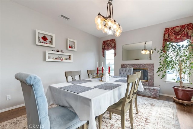 dining room featuring a fireplace, a wealth of natural light, hardwood / wood-style floors, and an inviting chandelier