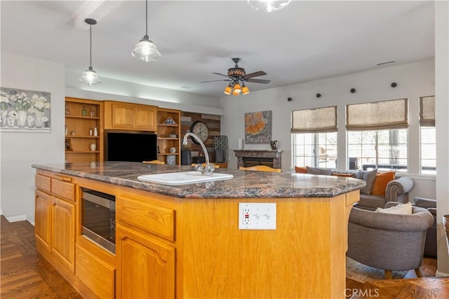 kitchen with stainless steel microwave, dark stone counters, a center island with sink, sink, and ceiling fan