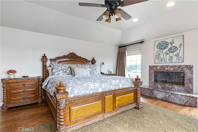 bedroom featuring a premium fireplace, ceiling fan, dark wood-type flooring, and vaulted ceiling